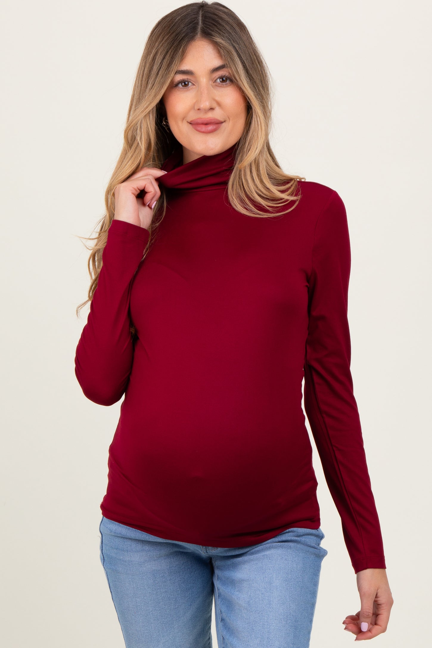 woman wearing a burgundy long sleeve maternity turtleneck top and showing her baby bump