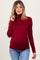 woman wearing a burgundy long sleeve maternity turtleneck top and showing her baby bump