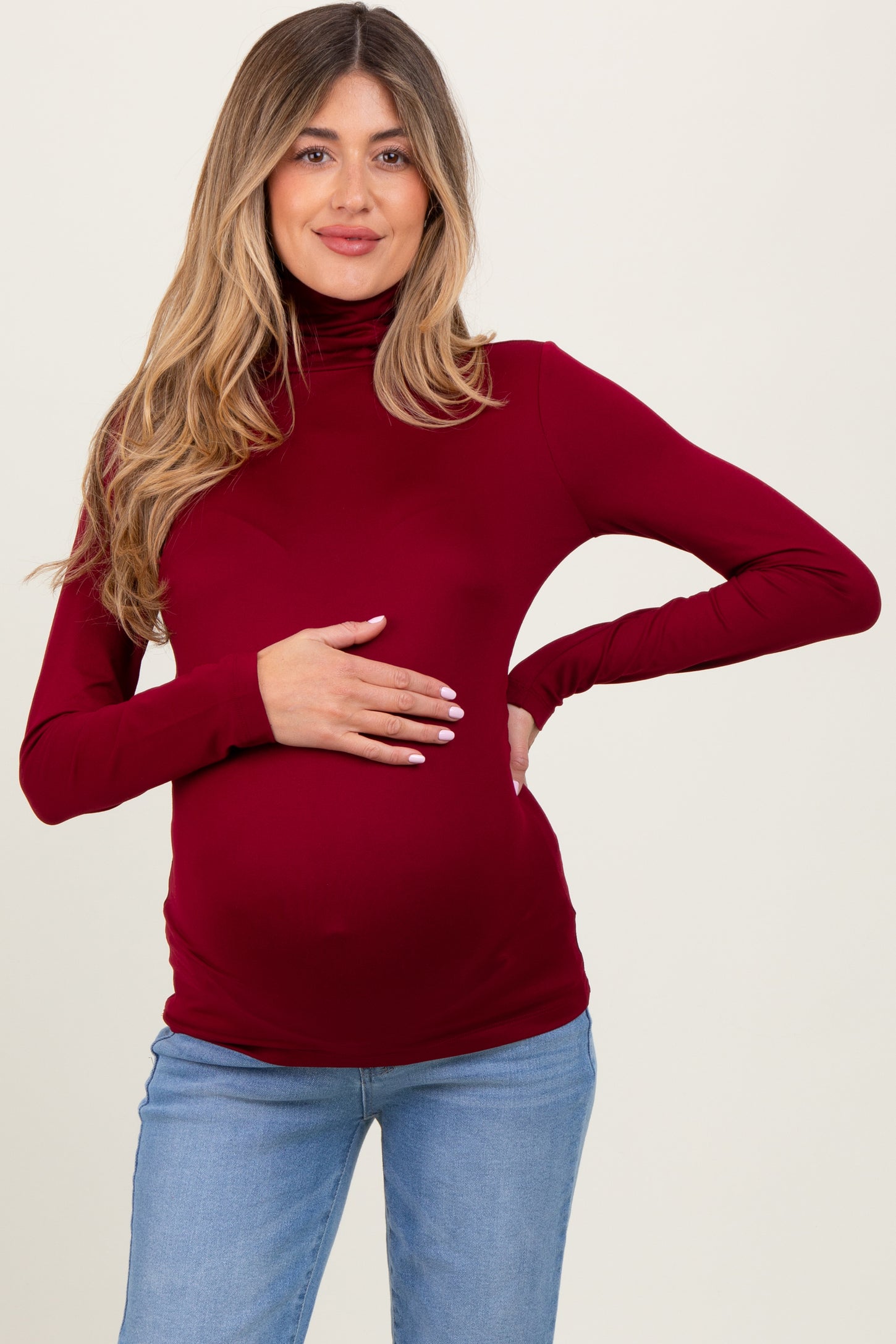 woman wearing a burgundy long sleeve maternity top and holding her baby bump
