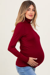 woman wearing a red long sleeve maternity turtleneck top and holding her baby bump