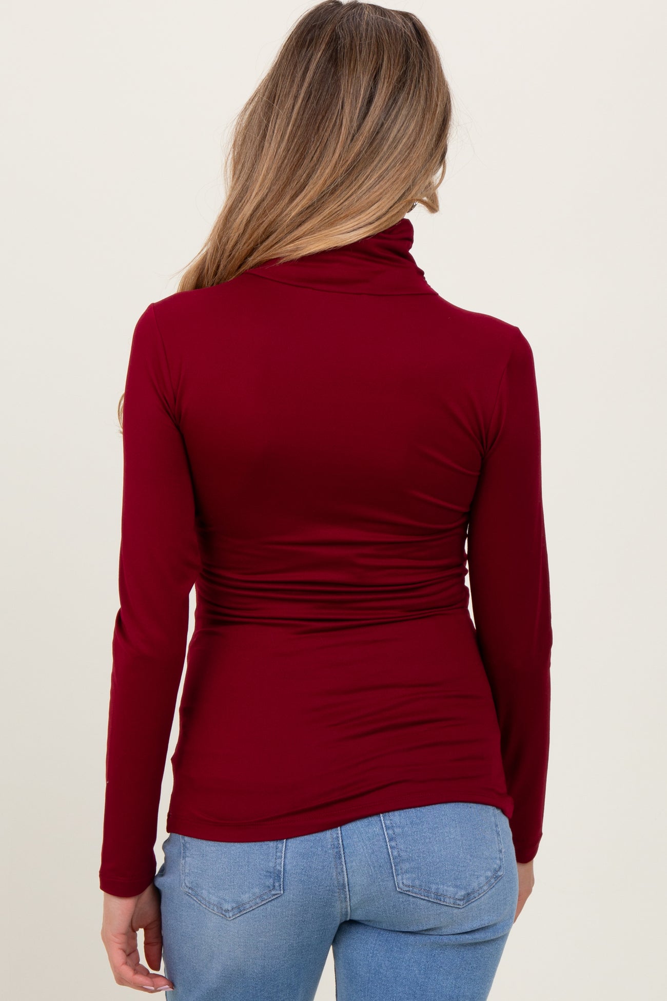 woman wearing a burgundy long sleeve maternity top with a cowl neck and gathered detailing at the waist