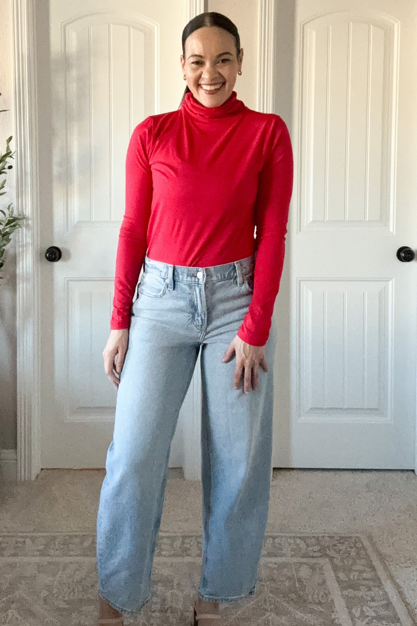 woman wearing a red long sleeve turtleneck top and high-waisted light blue wide-leg jeans