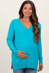 woman wearing a vibrant turquoise maternity sweater with a deep v-neck and side slits, cradling her baby bump