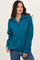 woman wearing a teal zip-up sweater with a textured knit pattern and long sleeves, smiling at the camera