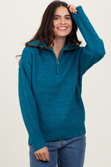 woman wearing a teal zip-up sweater with a textured knit design and a relaxed fit, smiling and posing with one hand in her hair