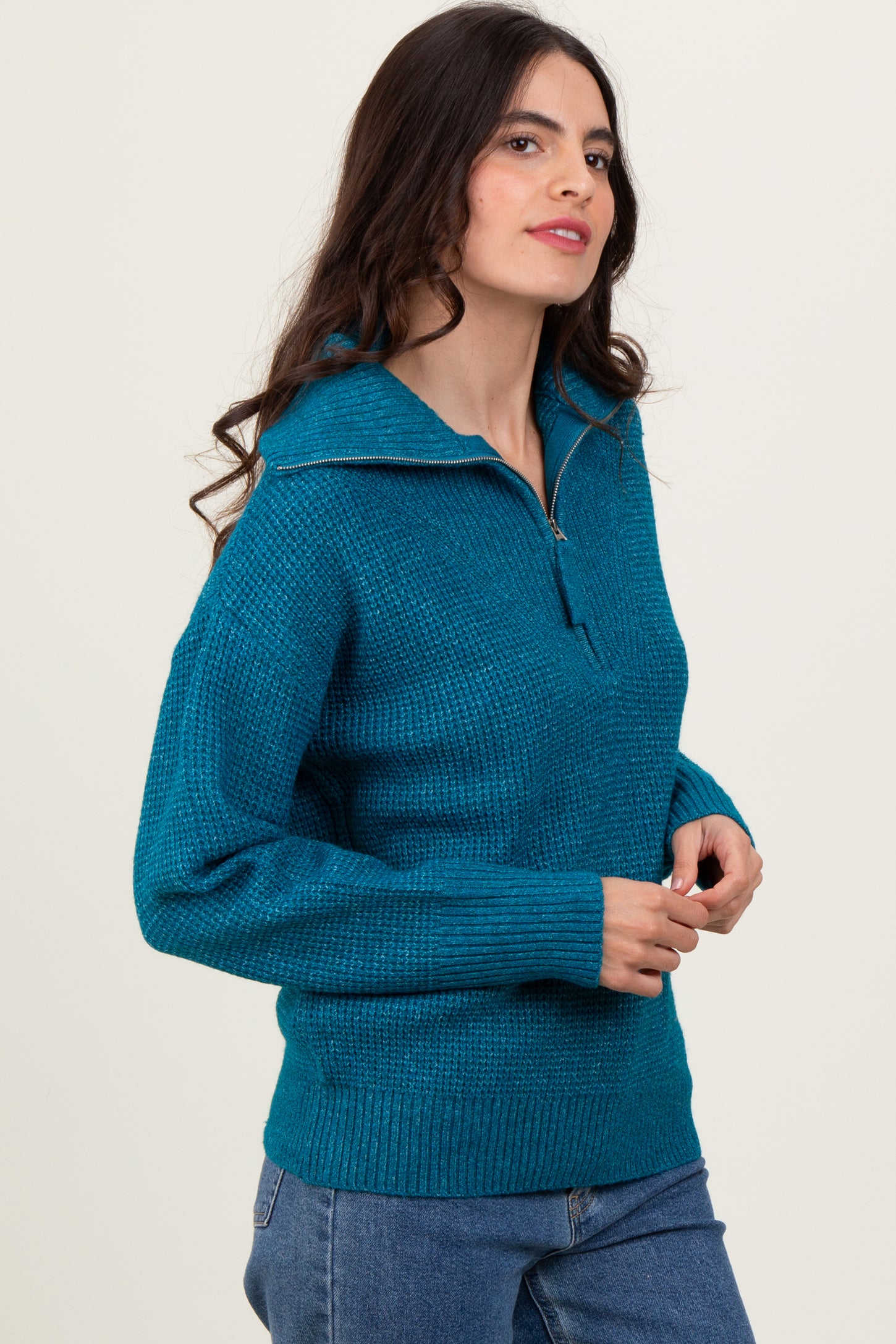 woman wearing a teal half-zip sweater with a textured knit and relaxed fit, standing against a neutral background