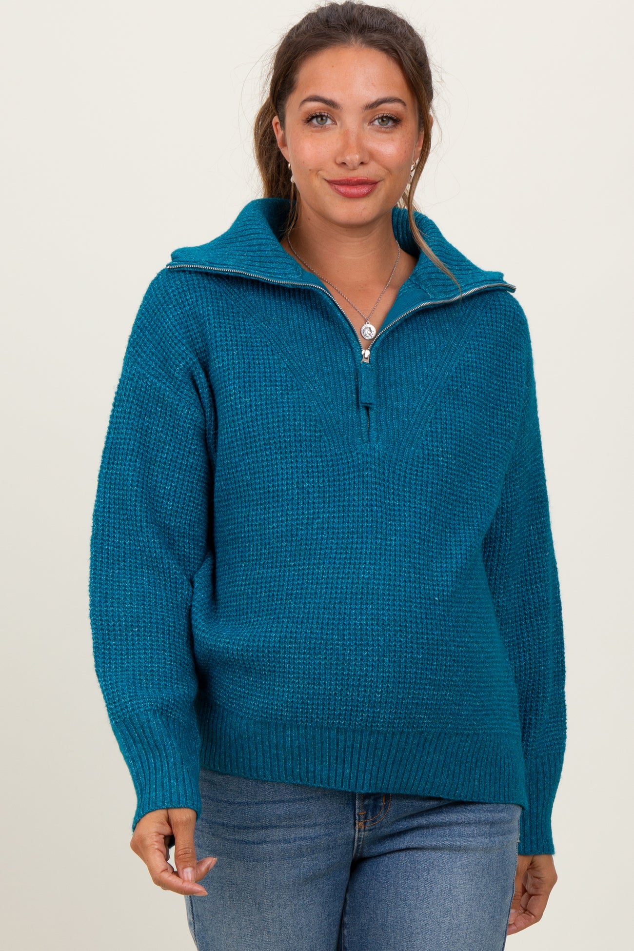 woman wearing a teal maternity pullover sweater with a half-zip and relaxed fit, showcasing her baby bump
