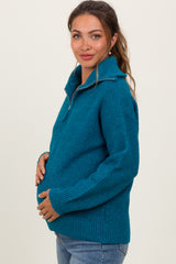 woman wearing a teal maternity sweater with a half zip and holding her baby bump