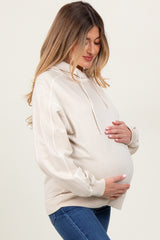 woman wearing a light beige maternity hoodie and holding her baby bump