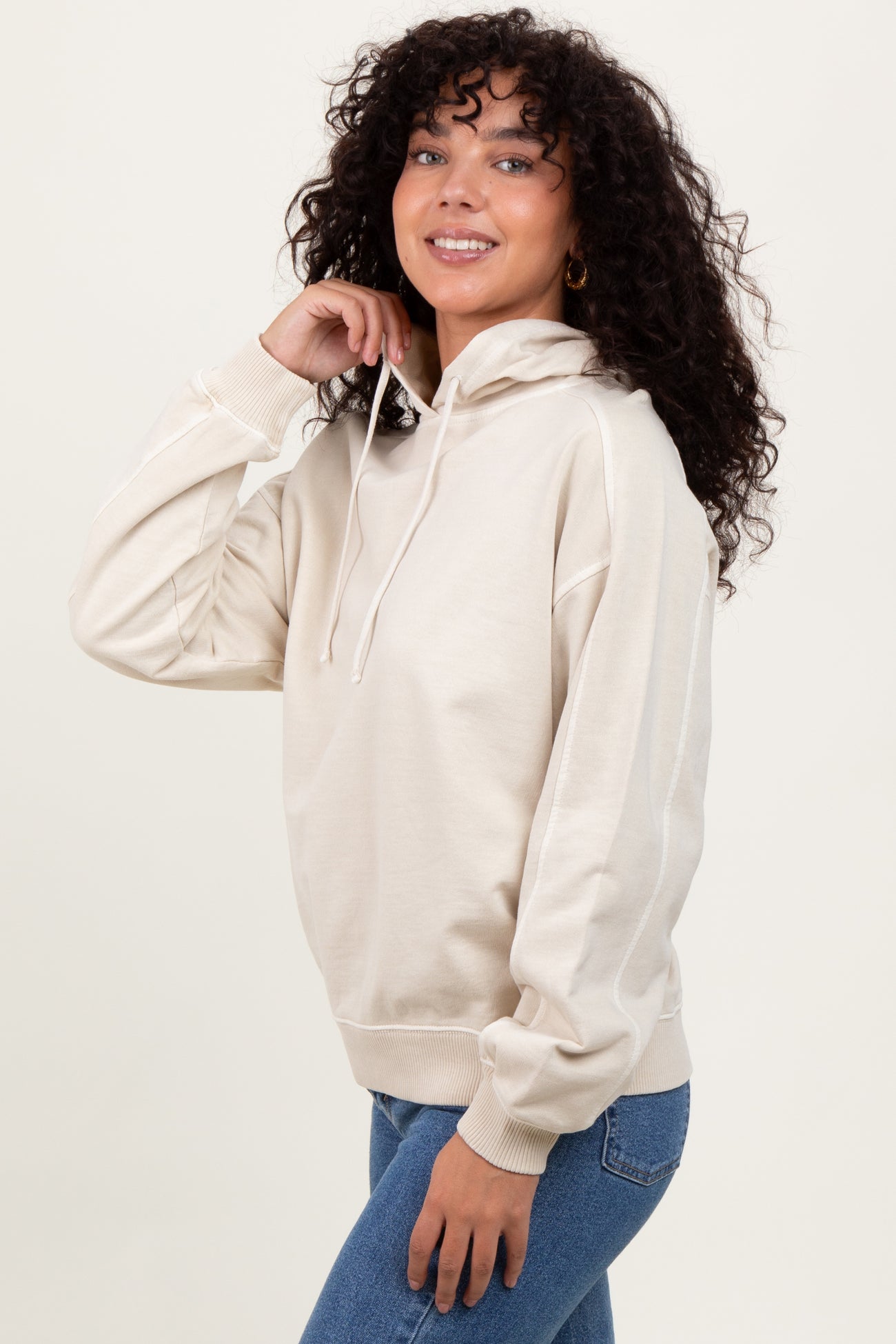 woman wearing a beige hooded sweatshirt with a relaxed fit and long sleeves, styled with blue jeans