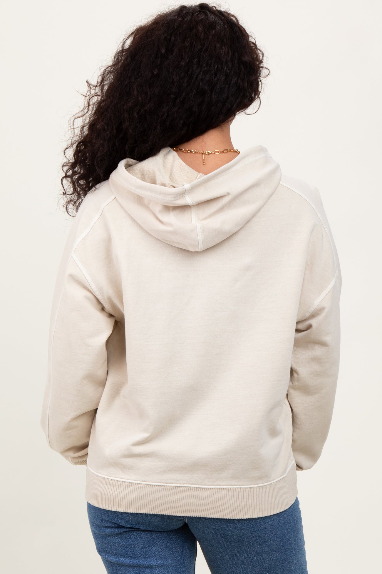 woman wearing a light beige oversized hoodie with a hood, seen from the back, paired with blue jeans