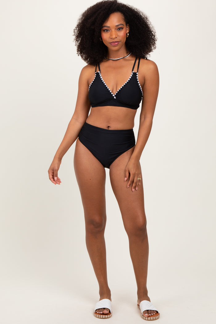 woman wearing a black bikini with embellished detailing and high-waisted bottoms, standing confidently