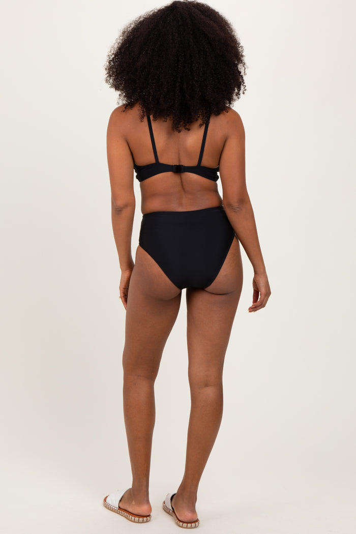 woman wearing a black bikini set with a strappy back and high-waisted bottoms, standing with her back to the camera