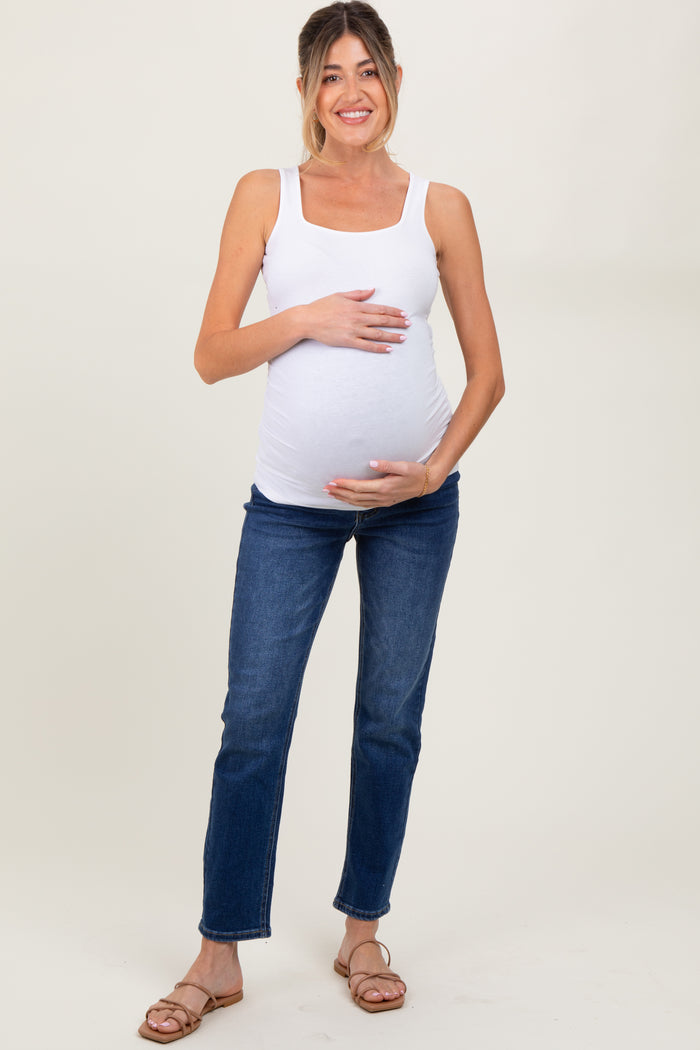 woman wearing a white maternity tank top and blue jeans, highlighting her baby bump with one hand on her belly
