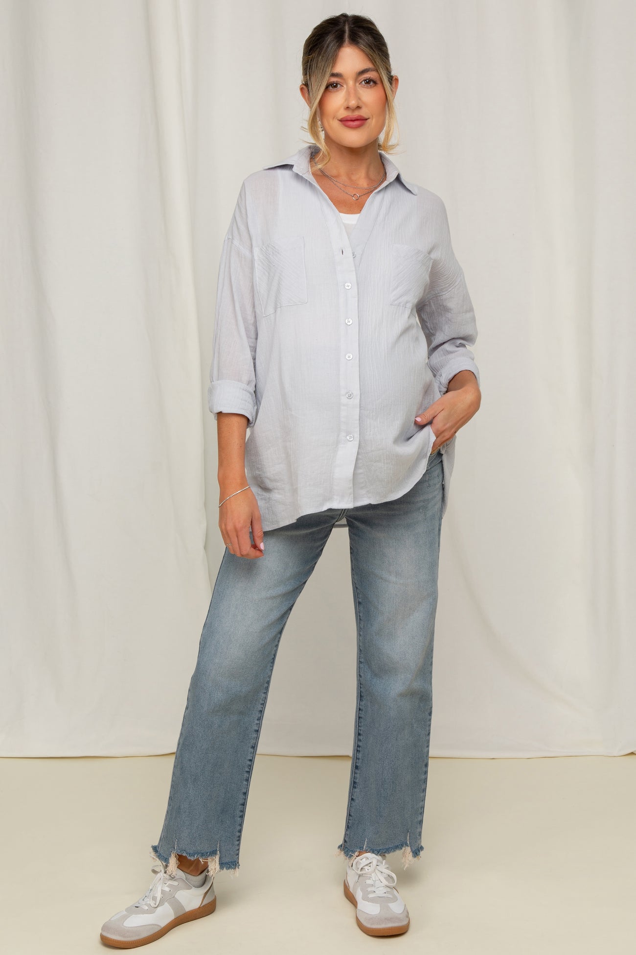 woman wearing a light blue maternity button-up shirt and distressed jeans, with a visible baby bump