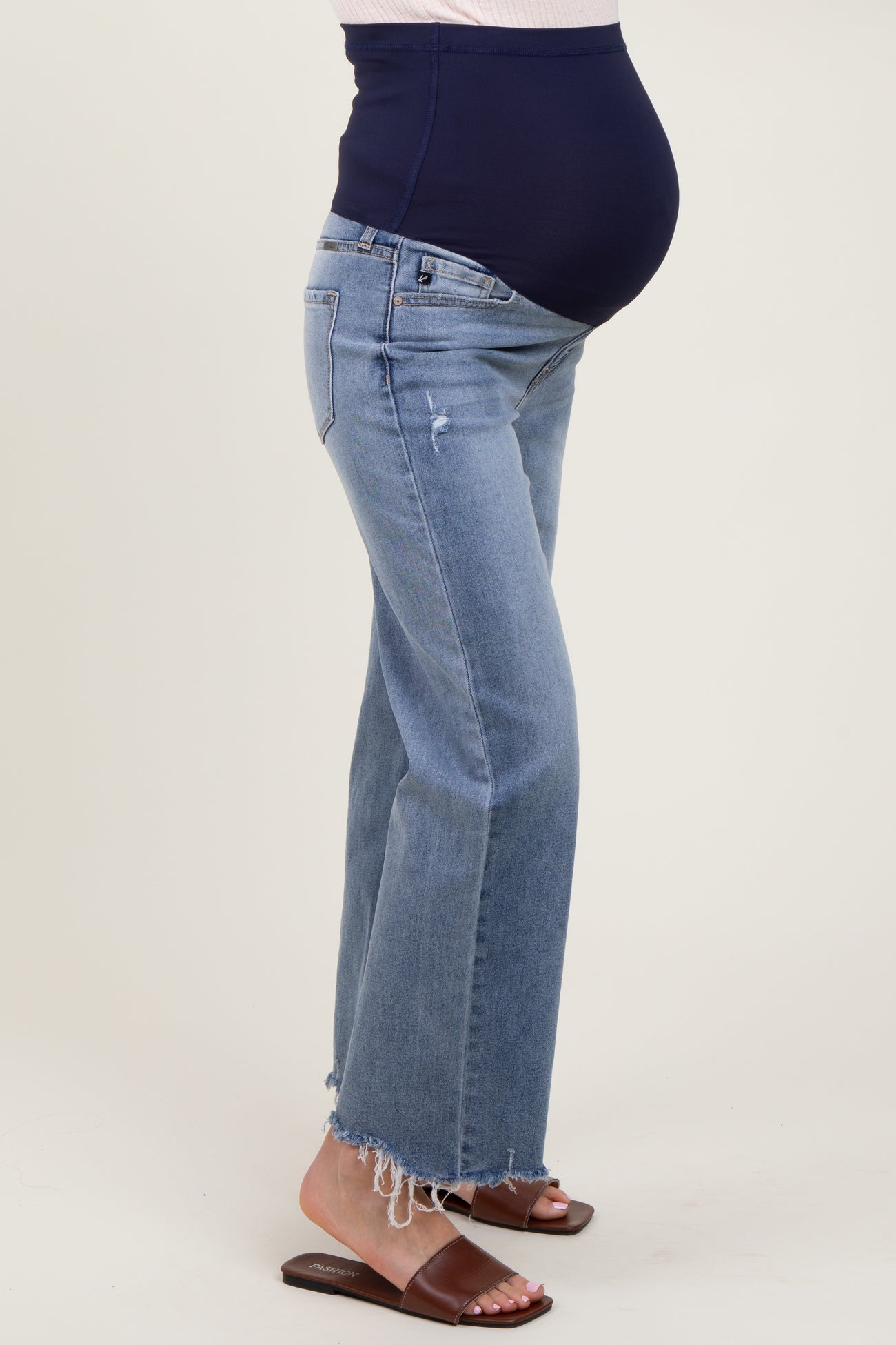 woman wearing light blue maternity jeans with a distressed hem and a navy blue over-the-bump waistband, showing her baby bump