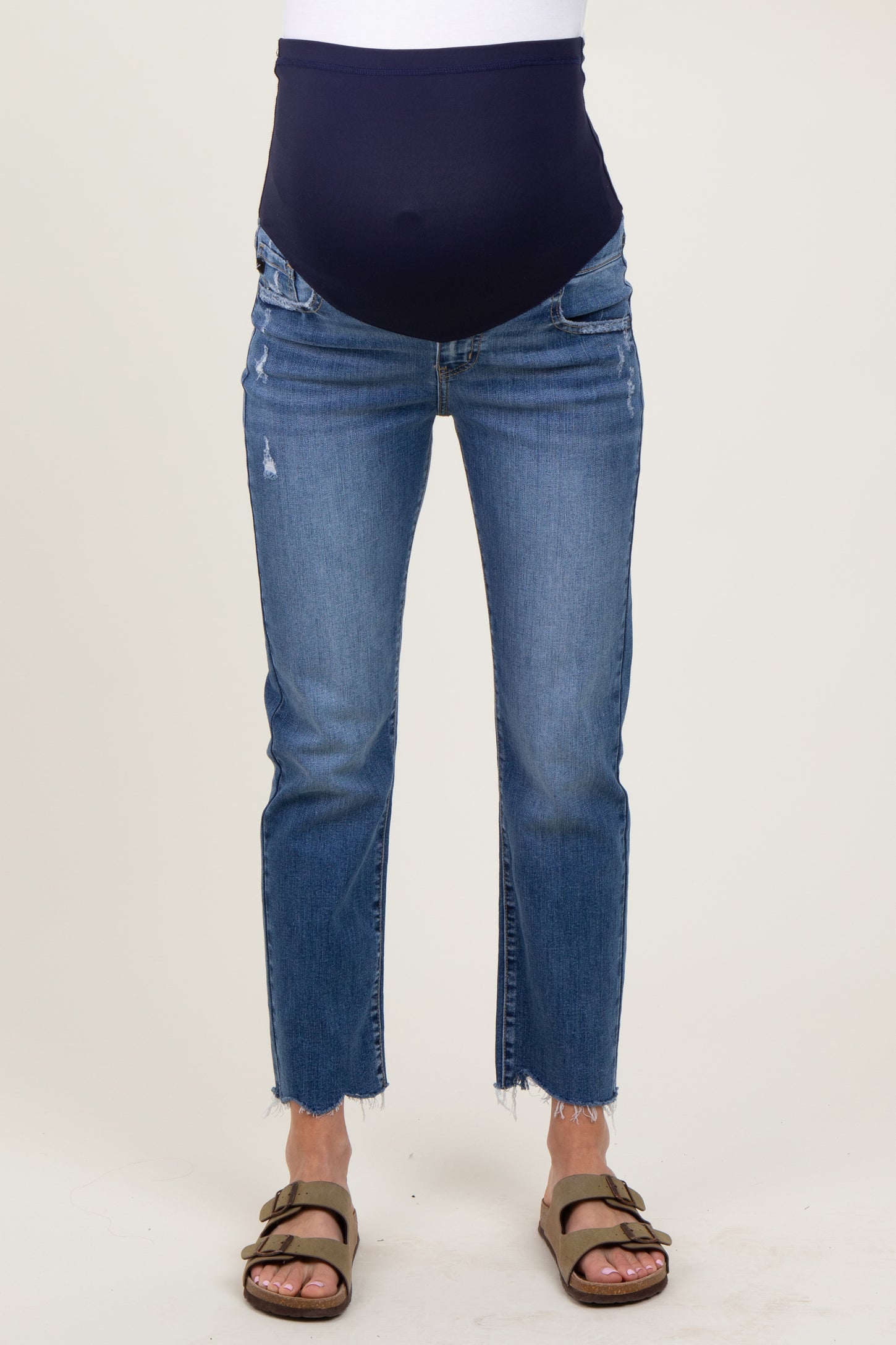 woman wearing a pair of distressed blue maternity jeans with a navy over-the-bump panel and side slits