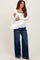 woman wearing a white long sleeve maternity top and blue wide-leg maternity jeans, holding a small white handbag, and showing baby bump