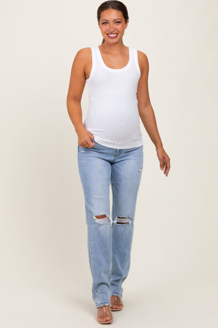 woman wearing a white ribbed maternity tank top and light blue distressed maternity jeans with a visible baby bump