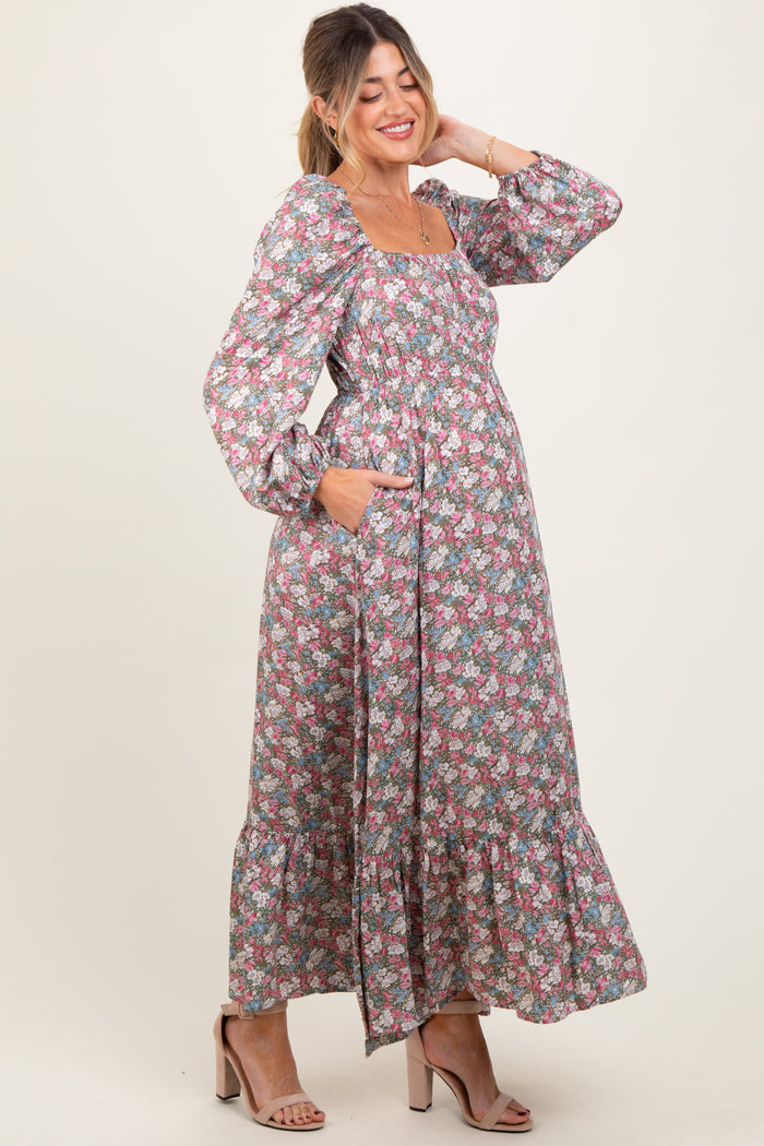 woman wearing a floral maternity maxi dress with long sleeves and pockets, smiling and showing her baby bump