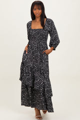 woman wearing a black floral maxi dress with a square neckline and puff sleeves, standing with hands in pockets