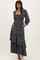 woman wearing a black floral maxi dress with a square neckline and puff sleeves, standing with hands in pockets