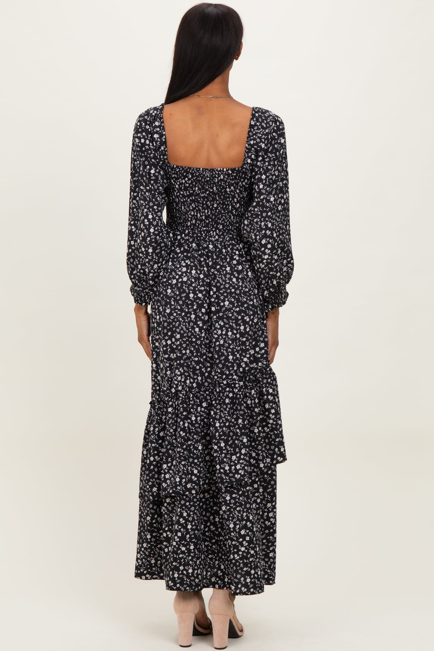 woman wearing a black floral long sleeve maxi dress with a square neckline and tiered skirt, viewed from the back
