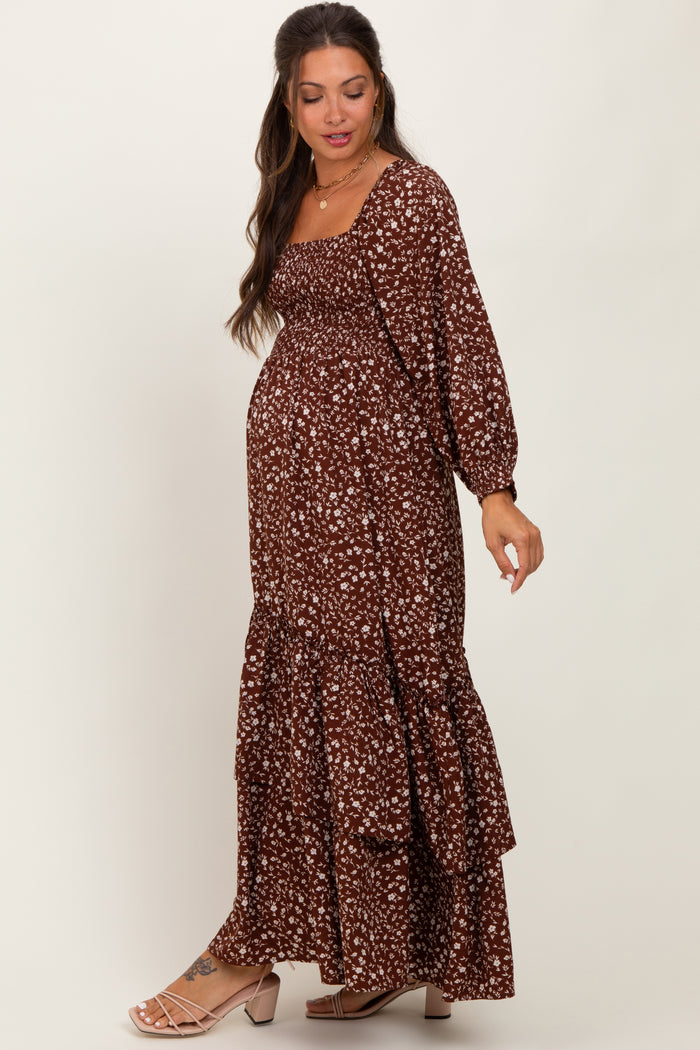 woman wearing a brown floral maternity maxi dress with long sleeves and ruffle details, showing her baby bump