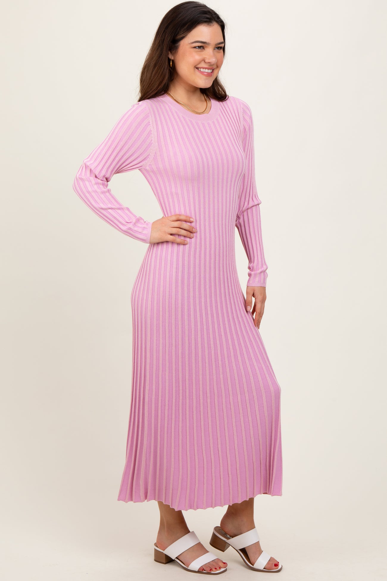 woman wearing a long pink ribbed knit dress with long sleeves and a fitted silhouette, standing with one hand on her hip