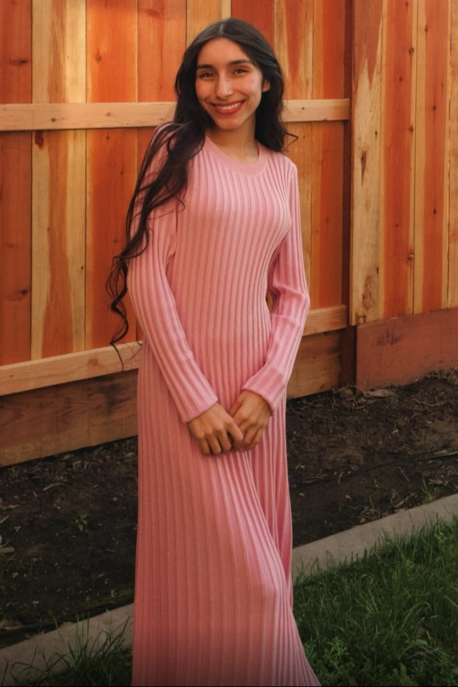 woman wearing a light pink ribbed long sleeve maxi dress standing in a garden area against a wooden fence