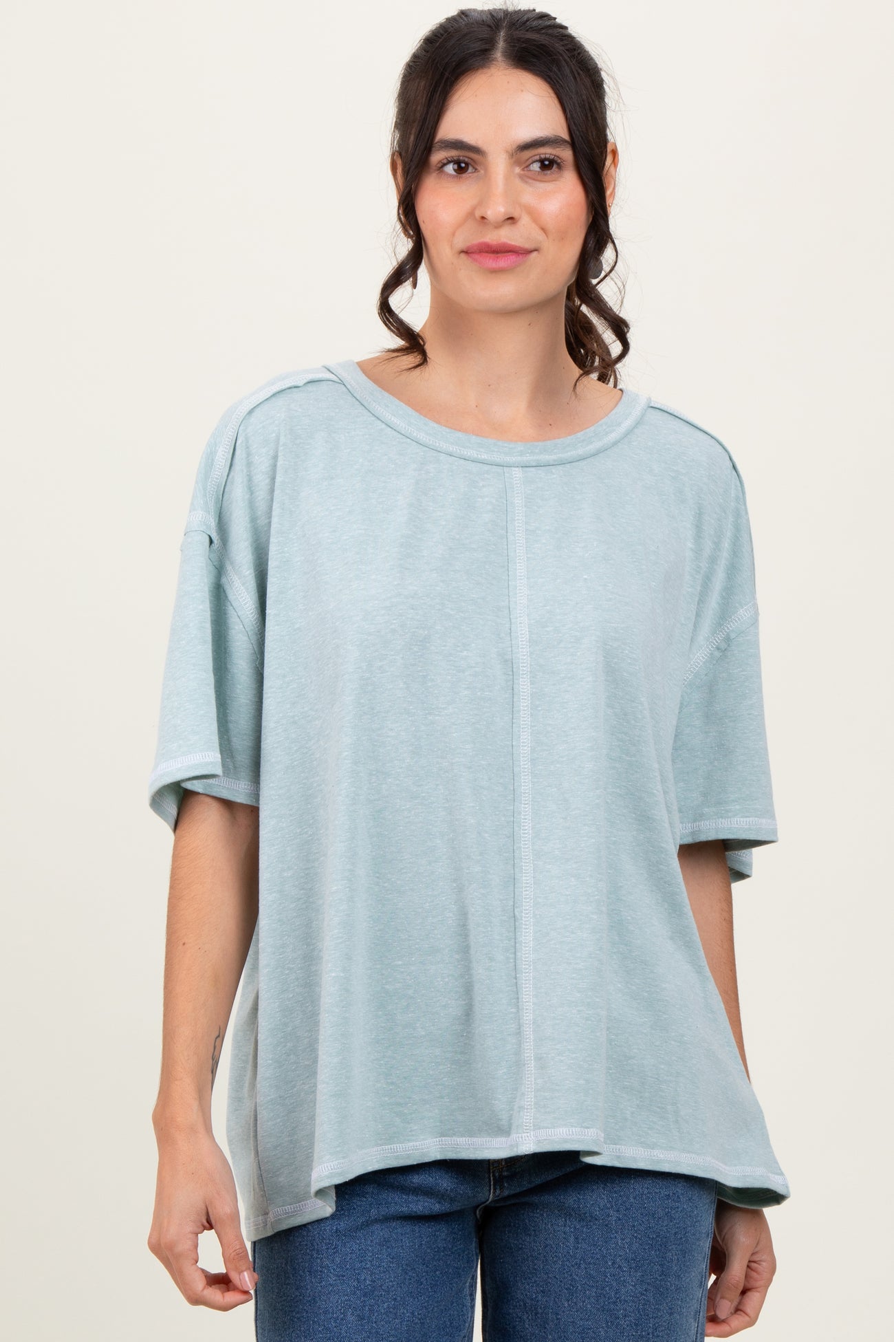 woman wearing a light teal oversized t-shirt with short sleeves and a relaxed fit, standing against a neutral background