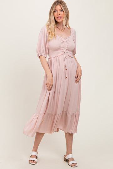 woman wearing a blush pink midi dress with puff sleeves and a cinched waist, standing against a light background