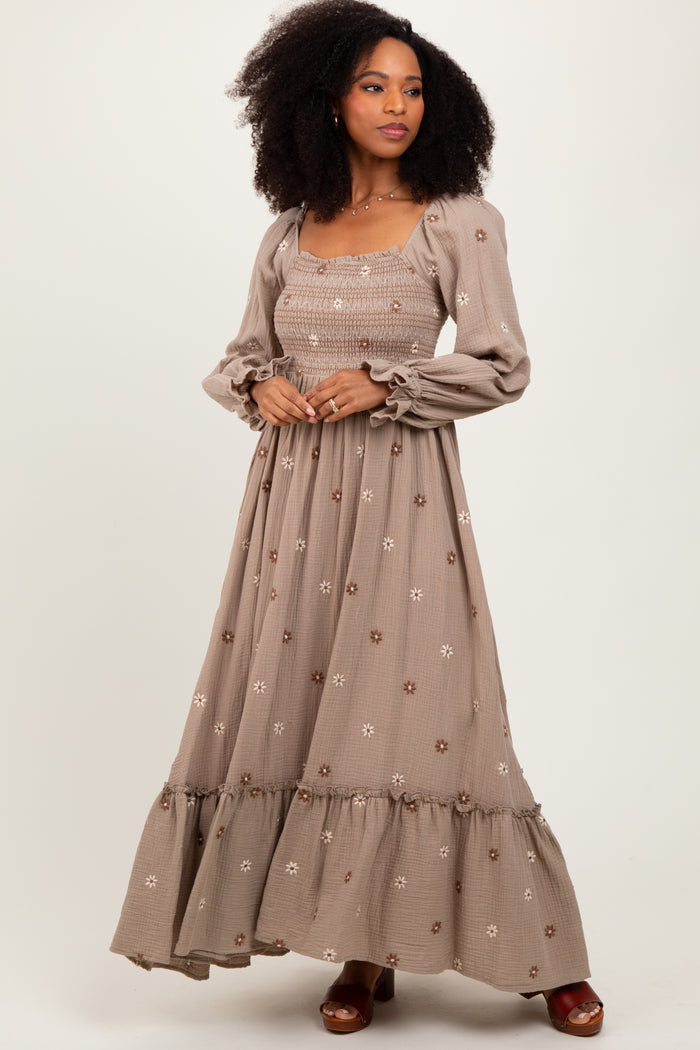 woman wearing a taupe long sleeve maxi dress with floral embroidery and ruffled hem