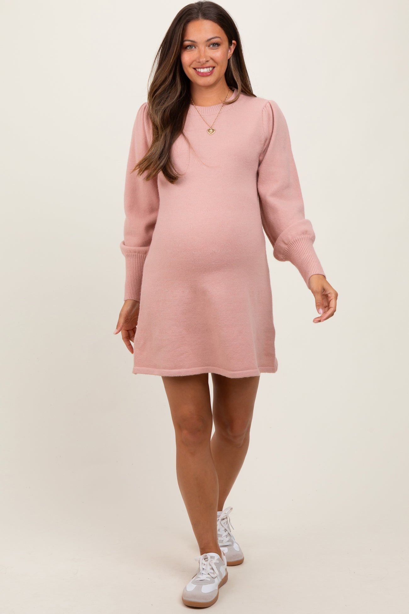woman wearing a light pink maternity sweater dress with puff sleeves and a visible baby bump