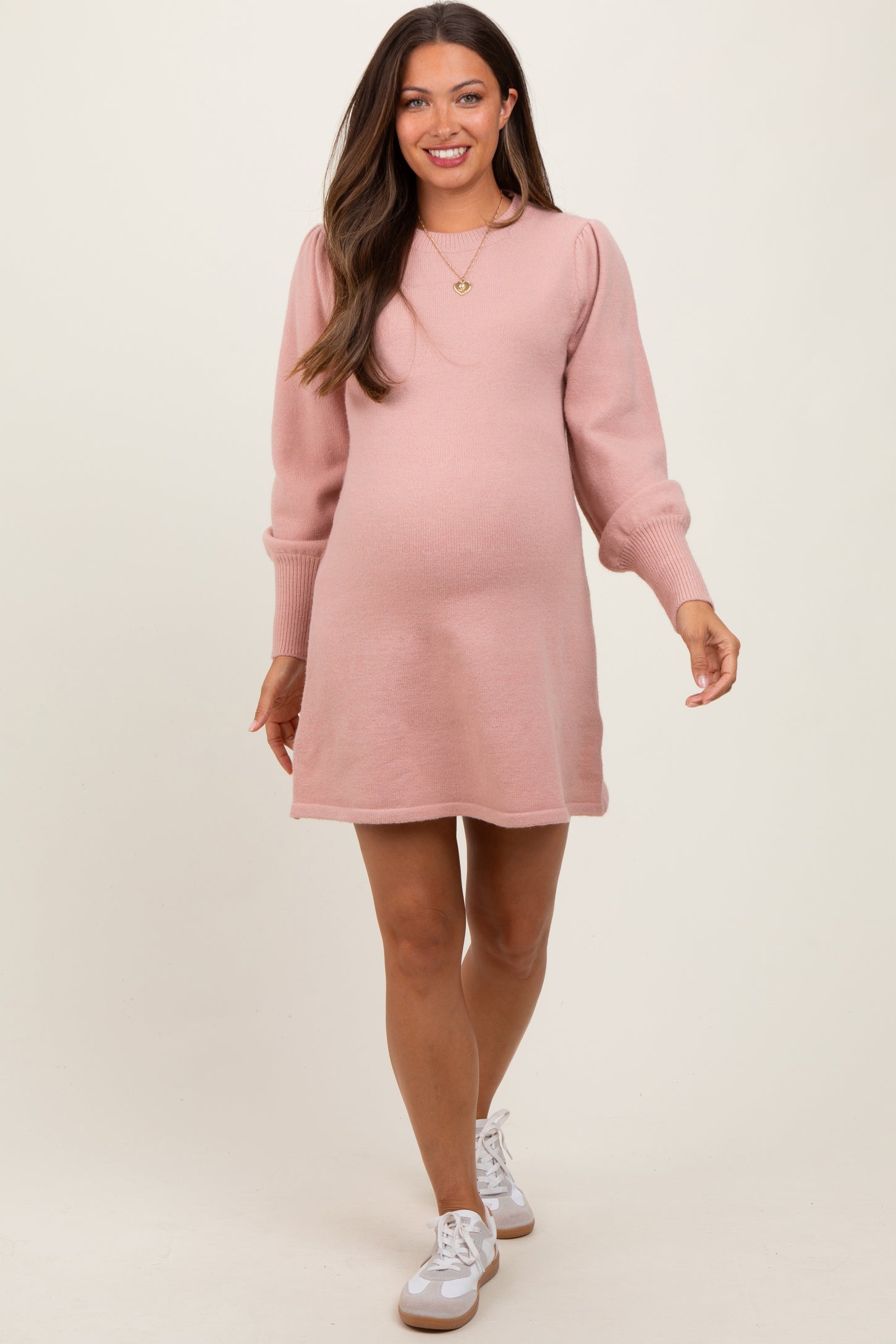 woman wearing a light pink maternity sweater dress with puff sleeves and a visible baby bump