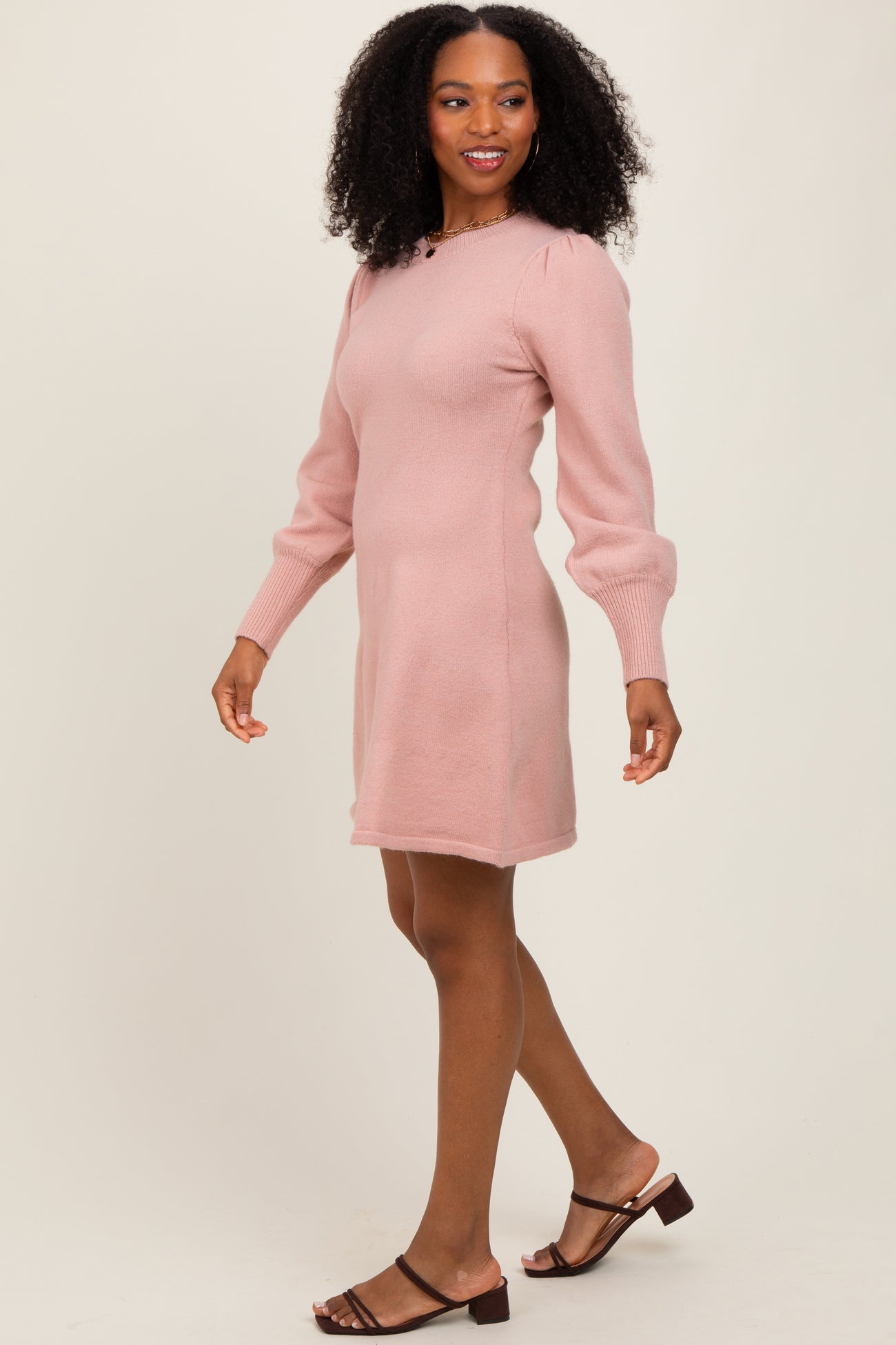 woman wearing a light pink long sleeve sweater dress with puffed sleeves and walking in a relaxed pose
