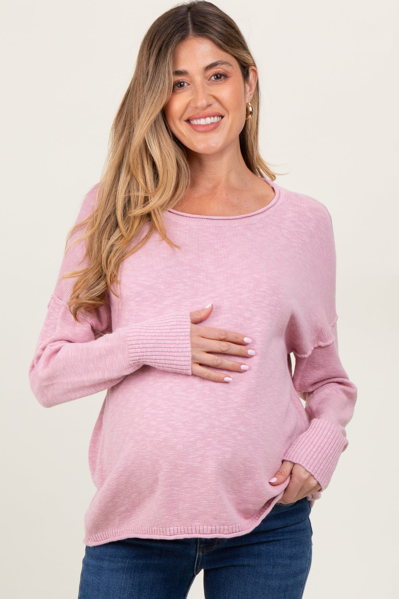 woman wearing a light pink maternity sweater and holding her baby bump