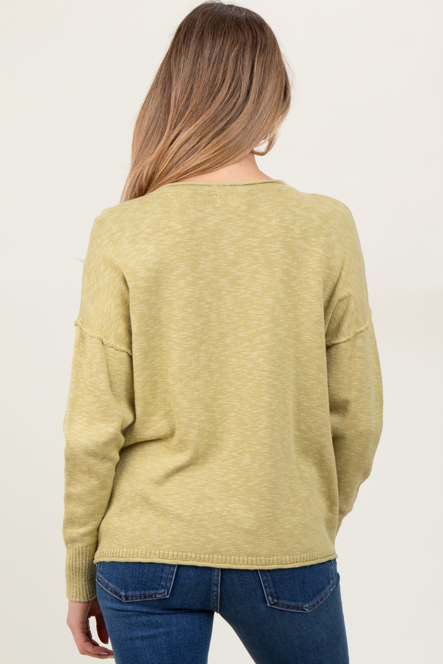 woman wearing a light green maternity sweater with a relaxed fit, seen from the back, paired with jeans