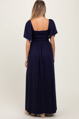 woman wearing a navy blue maternity maxi dress with short puff sleeves and a smocked bodice, showing her back