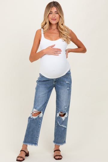 woman wearing a white maternity tank top and distressed blue maternity jeans, holding her baby bump