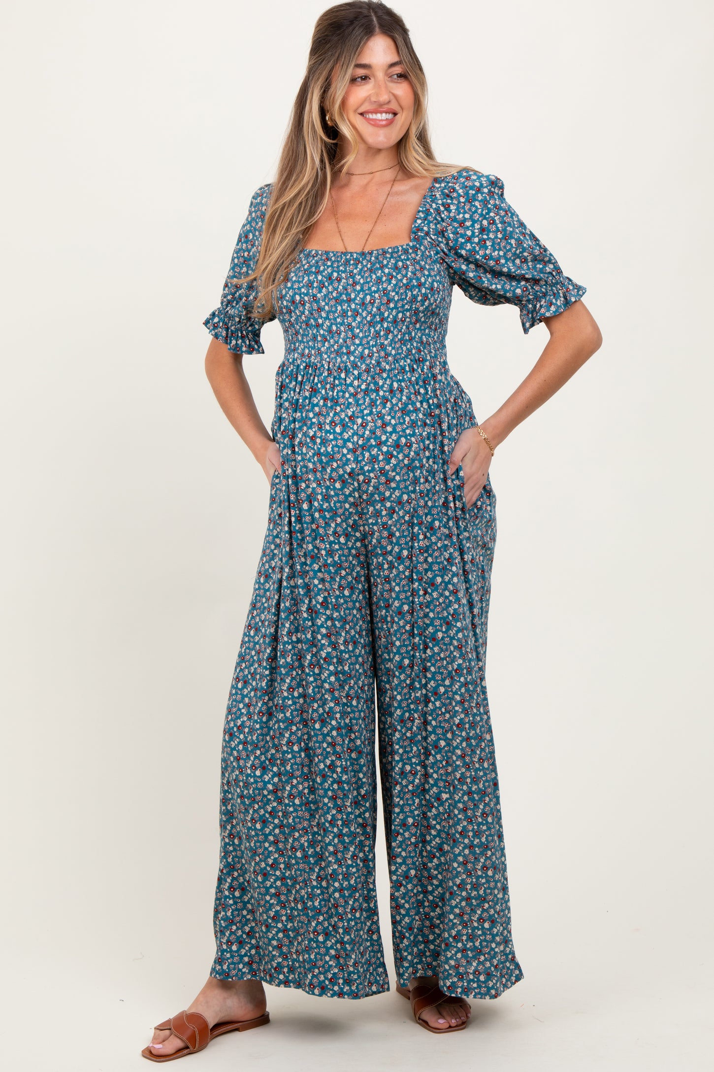 woman wearing a green floral maternity jumpsuit with short puff sleeves and pockets, showcasing her baby bump