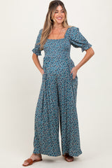 woman wearing a green floral maternity jumpsuit with short puff sleeves and pockets, showcasing her baby bump