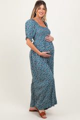 woman wearing a floral print blue maternity maxi dress and holding her baby bump