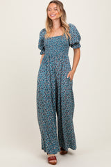 woman wearing a blue floral maxi dress with puff sleeves and pockets, smiling against a neutral background