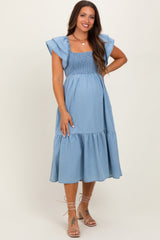 woman wearing a light blue maternity dress with smocked bodice and flutter sleeves, showing her baby bump