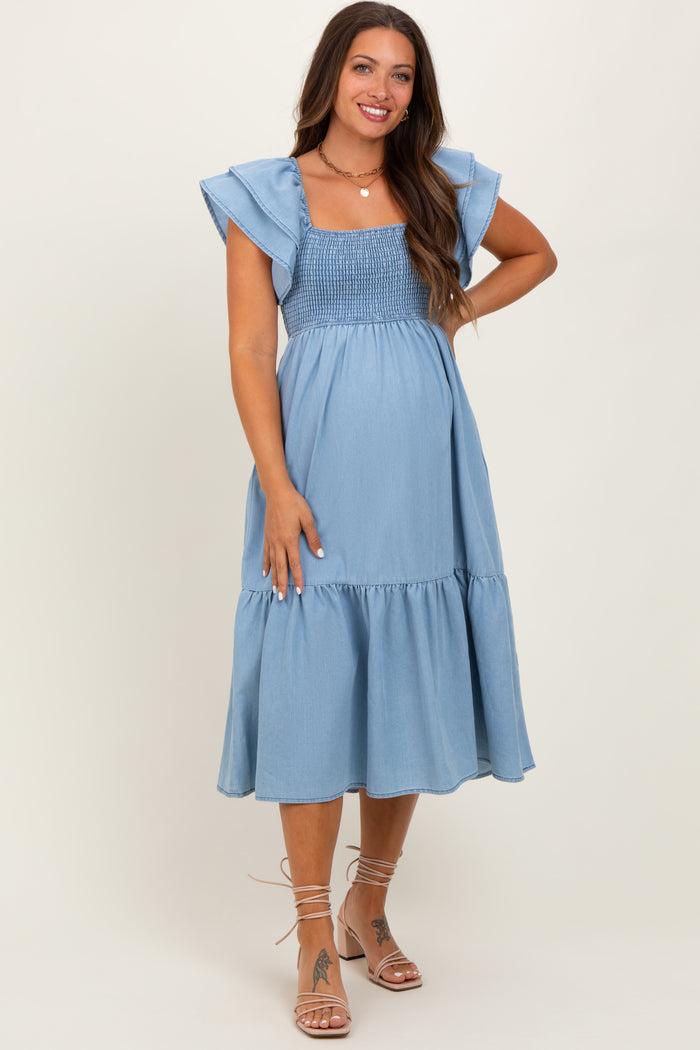 woman wearing a light blue maternity dress with smocked bodice and flutter sleeves, showing her baby bump