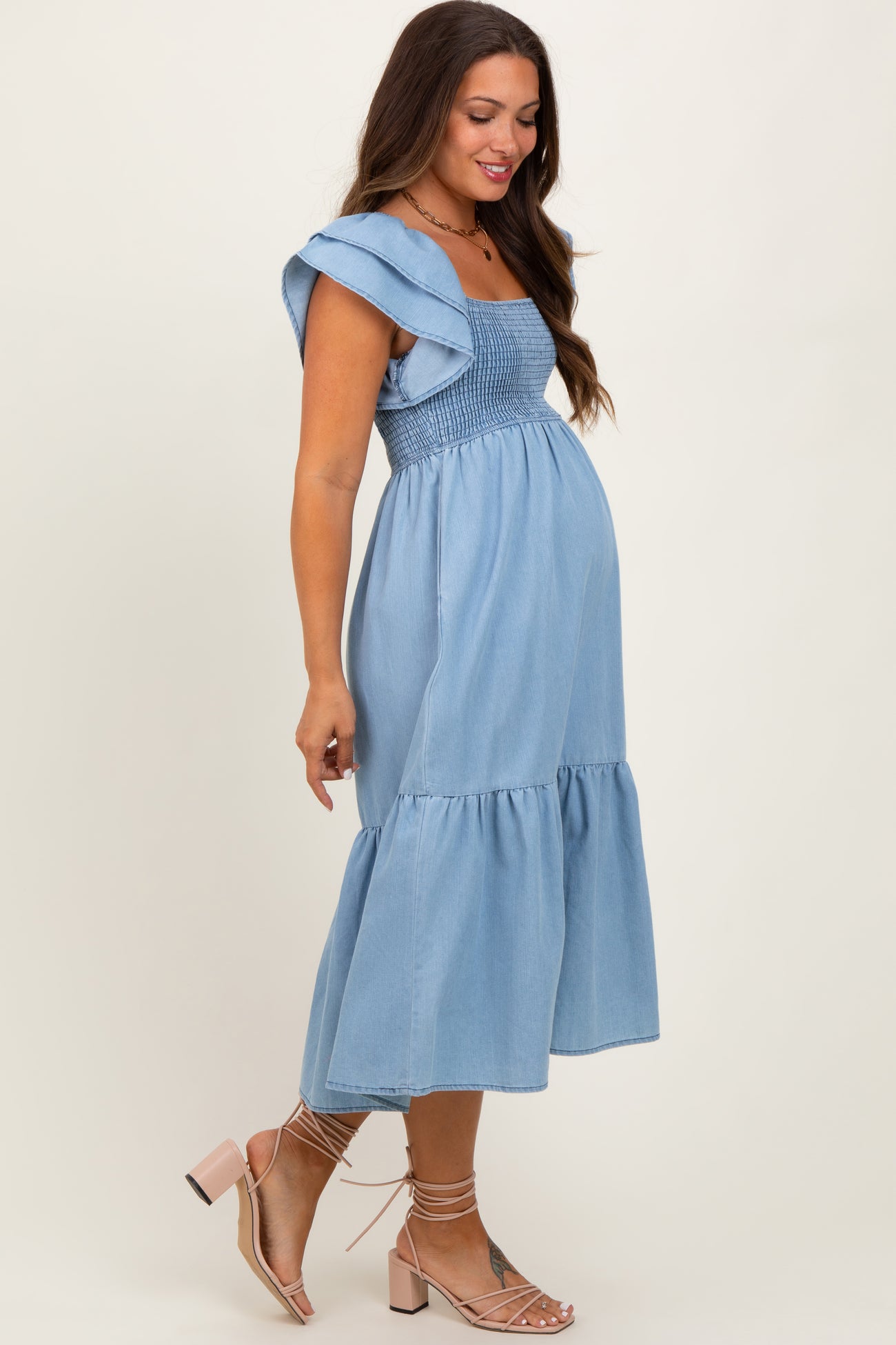 woman wearing a light blue denim maternity dress with a square neckline and ruffled sleeves, showing her baby bump