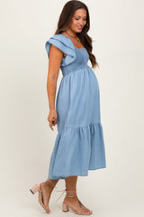 woman wearing a light blue denim maternity dress with a square neckline and ruffled sleeves, showing her baby bump