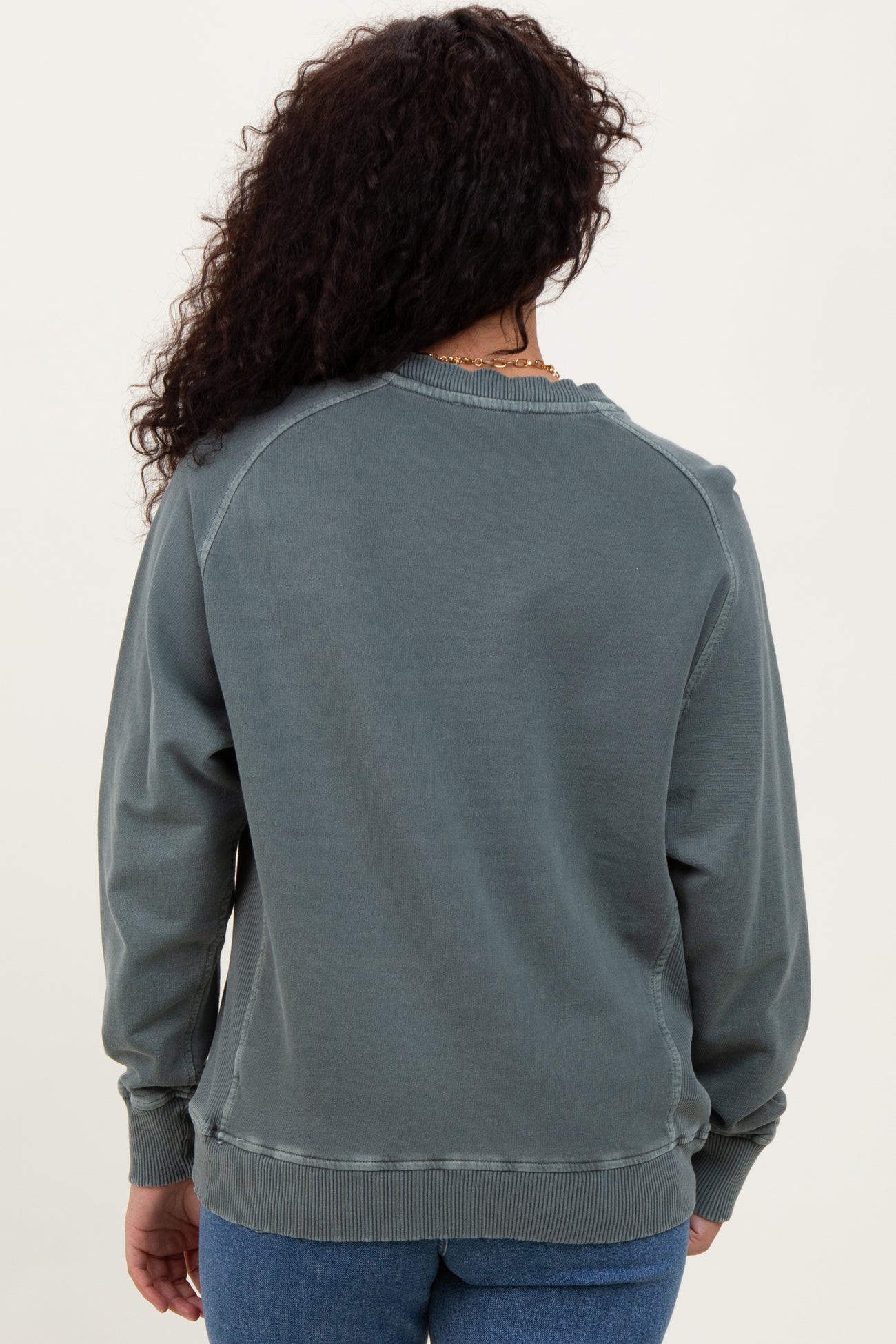 woman wearing a cozy green sweatshirt with a relaxed fit and ribbed cuffs, shown from the back