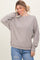woman wearing a light taupe oversized sweatshirt with ribbed detailing and relaxed fit, paired with blue jeans